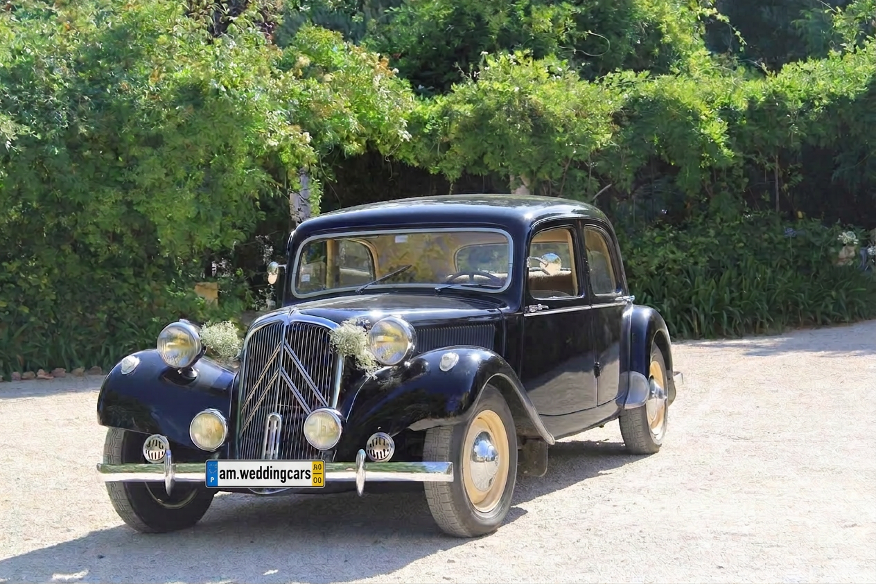 Citroën Traction azul-escuro decorado com flores brancas num jardim, com matrícula am.weddingcars