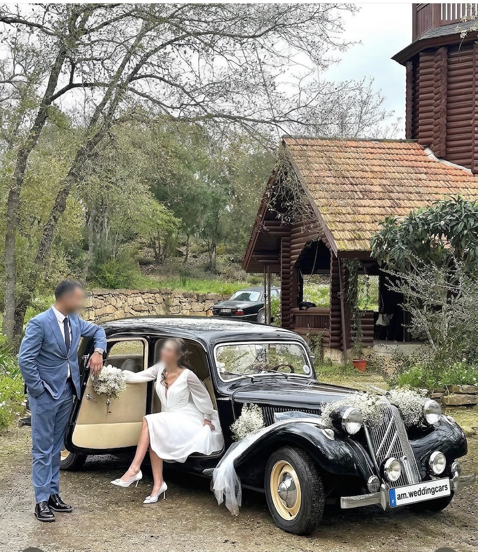 Noivos junto a Citroën Traction preto decorado com flores brancas em quinta rústica, com matrícula am.weddingcars